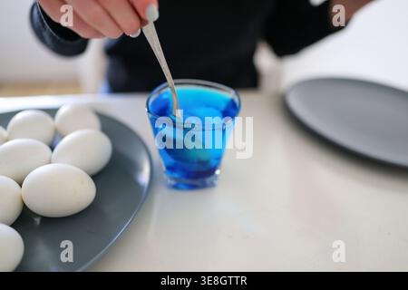 Coloring eggs in vibrant blue, festive preparation and creative kitchen moment. Stock Photo