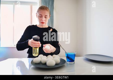Female hands decorating eggs, Easter preparation and DIY holiday activity in kitchen. Stock Photo