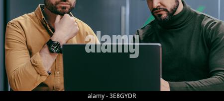 Two Men Focused on Working Together at a Laptop in an Office Setting Stock Photo