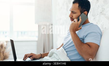 Man Talking on Phone While Using Laptop at Home in Morning Stock Photo
