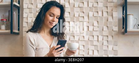 Young Woman Enjoys Coffee While Using Smartphone in a Cafe Setting Stock Photo