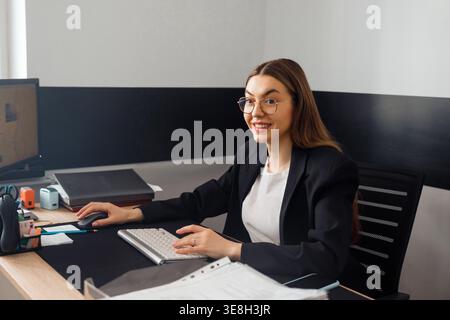 Woman working at office desk using computer and mouse. Business and corporate workplace concept. Female professional working in modern office environm Stock Photo