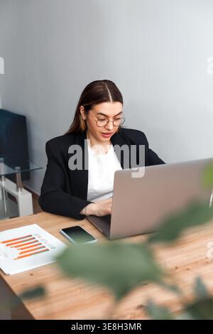 Woman working on laptop at office desk with documents. Beautiful businesswoman focused on tasks and workflow. Female professional working in modern co Stock Photo