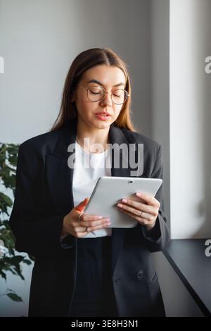 Woman using tablet at office desk. Attractive businesswoman working with digital device. Female professional using technology in modern corporate offi Stock Photo