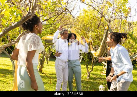 Friends celebrating two men embracing under arch with yellow boutonniere white shirts in garden Stock Photo