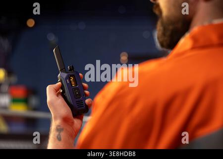 Close up of drilling barge technician using two way radio to coordinate emergency response procedures. Offshore platform employee communicating with technical team during night shift Stock Photo