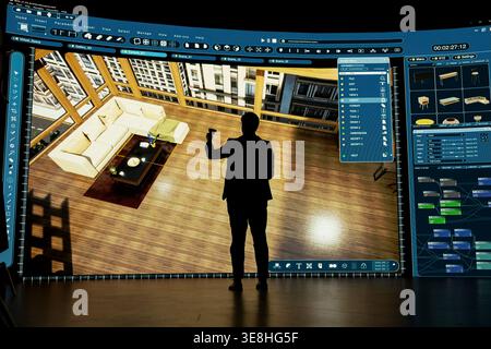 Architect uses virtual reality tech to design modern living room interior in CAD program. Designer holding VR controller interacts with 3D architectural model on large screen Stock Photo