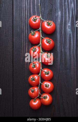 Vertical composition of cherry tomatoes on vine against dark wooden background. Fresh organic vegetables, minimal styling Stock Photo