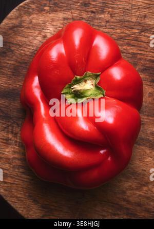 Single red bell pepper on wooden surface, top view. Fresh organic vegetable, minimal rustic styling Stock Photo