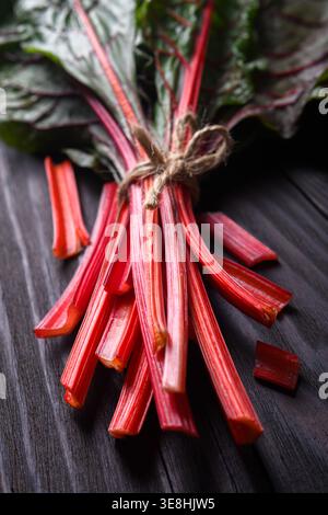 Fresh chard stalks tied with string on dark wooden surface, top view. Organic leafy vegetable with red stems Stock Photo