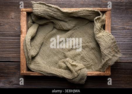 Empty wooden crate with linen cloth on rustic table, top view. Farm container mockup, food styling background Stock Photo