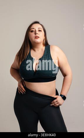 Body positivity concept. Beautiful plus size woman with curvy athletic physique poses confidently in studio wearing fitness clothing. Attractive femal Stock Photo