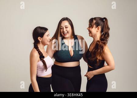 Friendship concept. Diverse women fitness friends including plus size curvy woman stand together in studio sportswear smiling and laughing. Female gro Stock Photo
