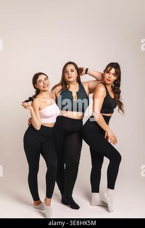 Inclusive wellness concept. Joyful diverse women fitness team including plus size curvy athlete poses full length in studio sportswear. Female group c Stock Photo
