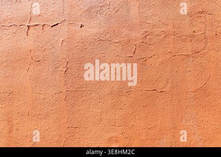 Orange textured wall with peeling paint. Terracotta colored stucco wall background. Close up of weathered plaster surface Stock Photo