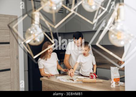 Family members work together in a kitchen to make food, showing a father helping his son while a mother watches. They have ingredients spread out and Stock Photo