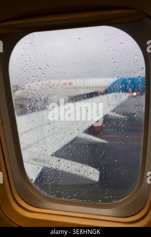View through airplane window with raindrops on glass and aircraft wing during rainy weather at airport Stock Photo