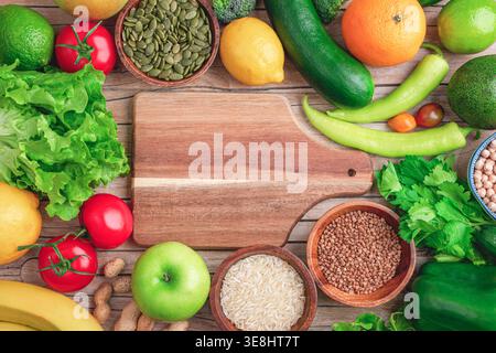 Healthy food background with vegetables, fruits and grains and cutting board on wooden surface. Top view, flat lay, mockup. Stock Photo