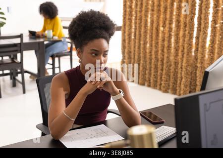Diverse female coworkers working in shared office, reviewing printed plans and using monitor Stock Photo