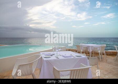 Elegantly set outdoor dining table in a seafood restaurant with white tablecloth, plates, cutlery, napkins and wine glasses on a seaside terrace overl Stock Photo