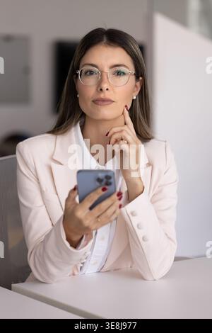 Confident businesswoman holding smartphone seated at office desk Stock Photo