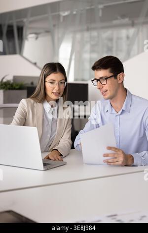 Coworkers discussing project details using laptop and papers Stock Photo