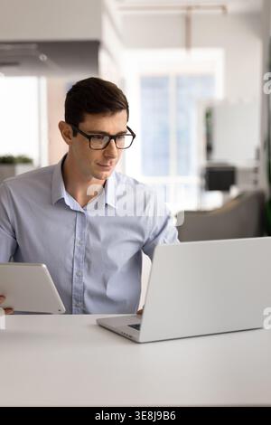 Man using laptop and holding digital tablet in office Stock Photo