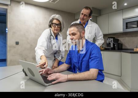 Medical professionals in scrubs and lab coats collaborating on a laptop, sharing information, and discussing healthcare data in a modern office or sta Stock Photo