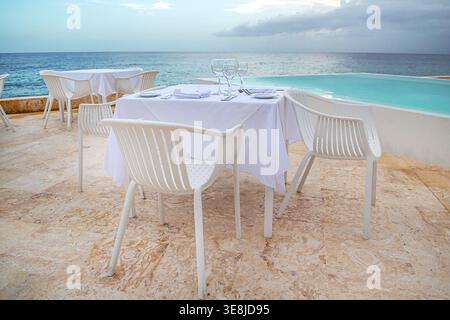 Elegantly set outdoor dining table in a seafood restaurant with white tablecloth, plates, cutlery, napkins and wine glasses on a seaside terrace overl Stock Photo