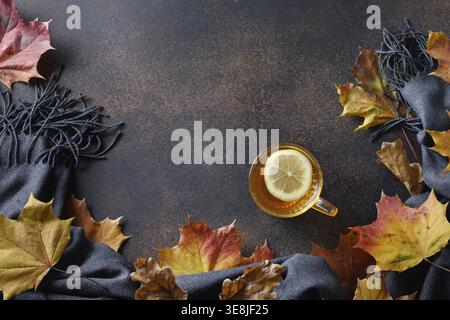 Cozy still life with warming tea, fall maple leaves and cozy scarf on brown background. View from above with copy space Stock Photo