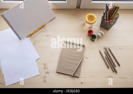 Creative workspace with notebook pencils paints and sketchbook on wooden desk top view for education art business and creative planning Stock Photo