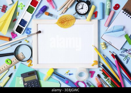 Wooden frame, alarm clock, different stationery and colorful supplies on blue background. Back to school concept. Top view Stock Photo