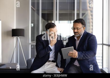 Two businessmen reviewing data, making information analysis on digital tablet Stock Photo