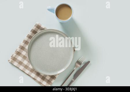 Empty ceramic blue plate, coffee and checkered napkin on plain light blue background. Table setting for breakfast. Mock up. View from above. Copy spac Stock Photo