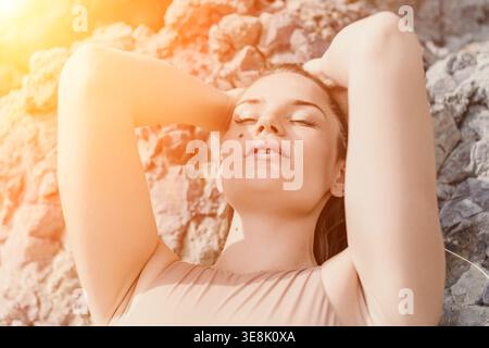 Woman relaxation sunbathing rests against rocky cliff with eyes closed in warm golden sunset light Stock Photo