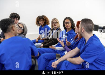 Diverse group of healthcare students and professionals in scrubs engaging in a collaborative discussion, sharing ideas and knowledge during a medical Stock Photo