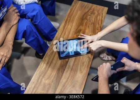 Medical professionals discussing patient care, zooming in on an x ray image showing a hip bone on a digital tablet during a consultation, illustrating Stock Photo