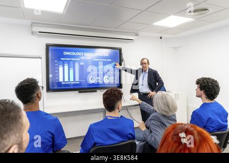 Oncologist presenting oncology data and survival rate charts on a large screen to diverse healthcare students and colleagues during a seminar focused Stock Photo