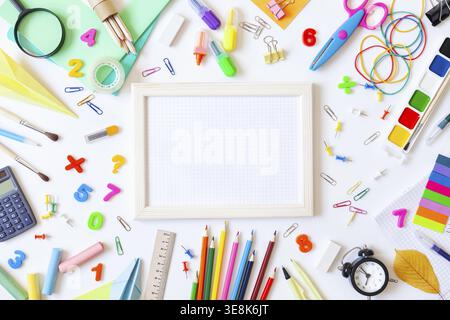 Empty wooden frame with squared paper, alarm clock, different stationery and colorful supplies on white background. Back to school concept. Top view Stock Photo