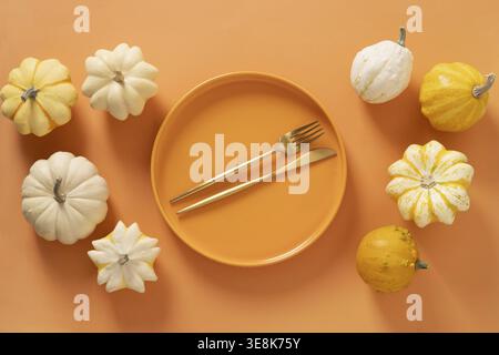Autumn composition of colorful different small pumpkins, orange empty plate with golden cutlery on orange background. Harvest day, Concept catering or Stock Photo