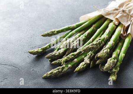 Bunch of fresh green asparagus sprouts in craft paper grocery bag on stone table. Healthy and diet food Stock Photo