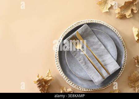 Autumn grey table setting decorated dry oak leaves and golden cutlery on beige. View from above. Banner for Thanksgiving day Stock Photo
