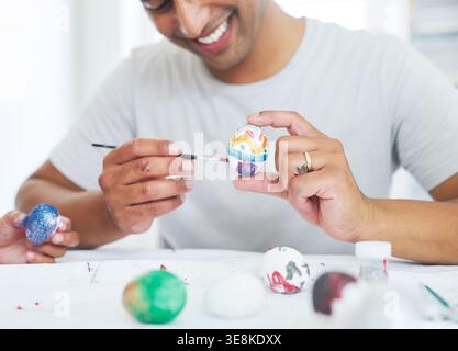 Hands, paintbrush and easter eggs with decoration in home with stroker, process and smile with creativity. Happy man with painting, art and Stock Photo
