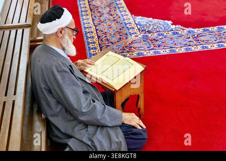 A man sits on the floor of Fatih Mosque in Istanbul Turkey, reading from the Quran. The space is rich with culture and religious practice Stock Photo