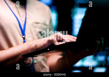 Meticulous technician doing checkup, inputing data on tablet of needed fixes in server hub housing advanced data storage infrastructure supporting critical IT workloads, close up Stock Photo