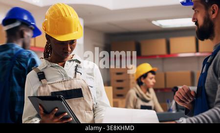 Multiethnic team of workers analyzing stock list on tablet, looking at delivery service cargo to ship merchandise. Young people scanning barcodes for inventory, industrial scanner. Handheld shot. Stock Photo