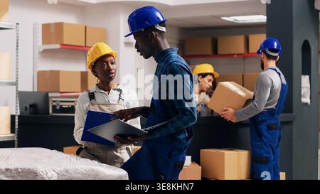 African american people doing quality control in warehouse, working with merchandise from depot shelves. Team of man and woman checking products for industrial service. Handheld shot. Stock Photo