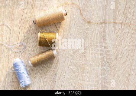 Colorful thread spools and sewing needles lying on a wooden surface, representing craft, hobby, and textile work Stock Photo