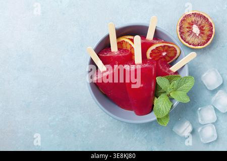 Homemade citrus ice cream or popsicles decorated mint and orange slices on blue table from above. Frozen fruit juice. Summer food Stock Photo