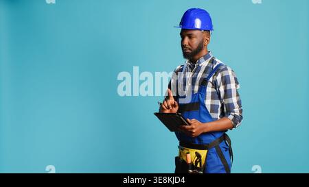 Confident mechanic using tablet for calculations and industrial measurements in studio. Young professional builder searching for construction inspiration online on gadget, contractor. Stock Photo